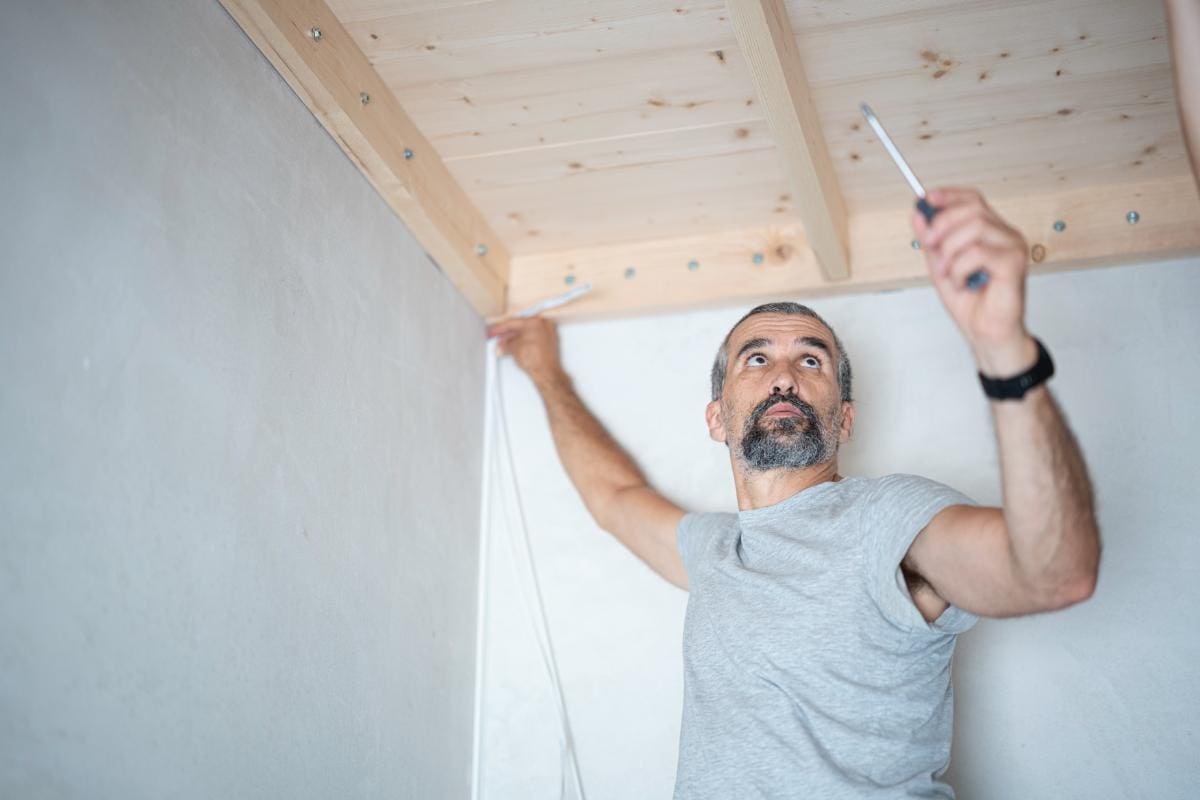 Man installing wooden ceiling with tools.