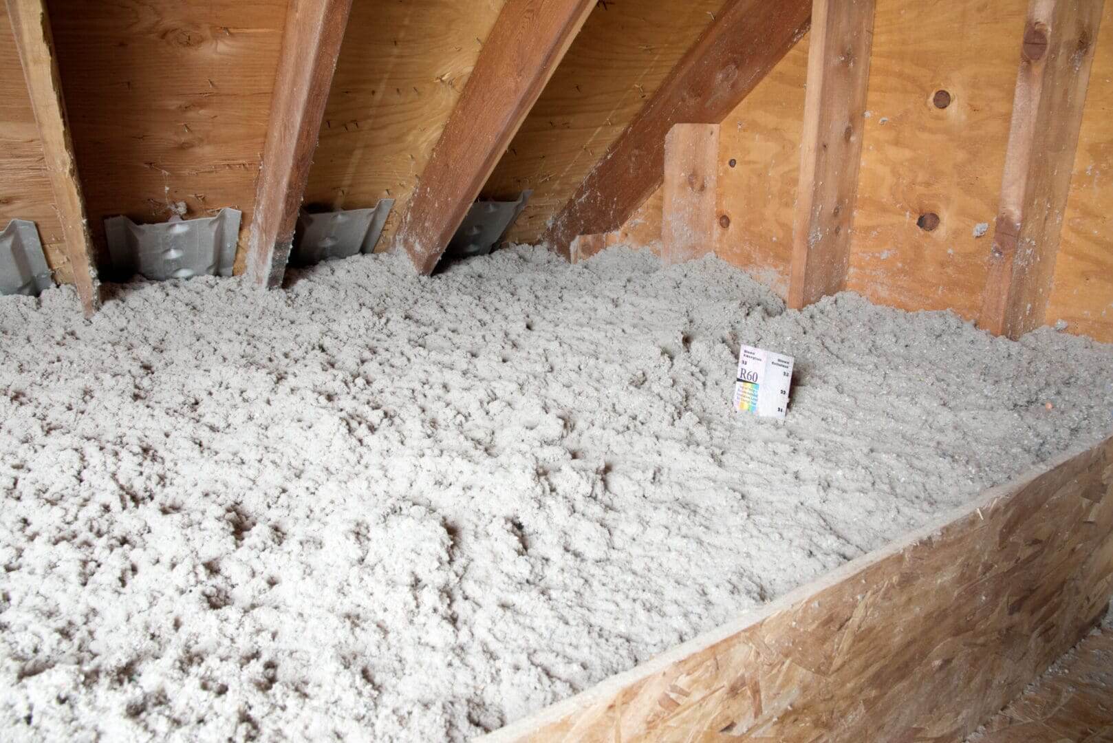 Attic with loose-fill insulation and wooden beams.